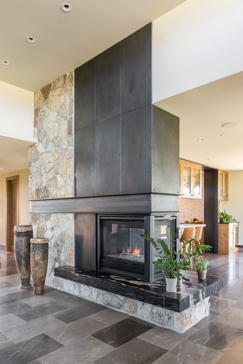 Steel + Stone double sided fireplace. Large African drums, plants, tile floor Double Sided Fireplace Kitchen Living Room, Mid Century Modern Double Sided Fireplace, Double Sided Fireplace Between Kitchen And Living Room, Double Sided Chimney, Double Sided Fireplaces, Four Sided Fireplace, Stone Fireplace Halfway Up Wall, 4 Sided Fireplace, Double Sided Fireplace Bedroom