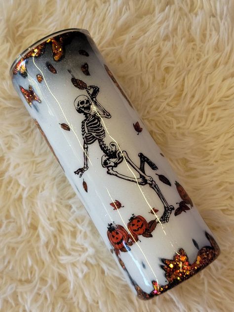 20 oz stainless steel tumbler is glitter in a gorgeous autumn orange color then distressed effect added on top and finished off with a decal of a happy skeleton enjoying falling leaves with a row of pumpkins at his feet. Cup is perfect for both the spooky season and fall lover. The double walled tumbler will keep your drink hot or cold for hours. Perfect for use year round. Please allow up to 2 weeks for processing and shipping as this is made at time of purchase. Halloween Themed Tumblers, Skeleton Tumbler Ideas, Halloween Tumbler Cup Ideas, Fall Tumbler Designs, Orange Glitter Tumbler, Spooky Tumbler Cup, Halloween Glitter Tumblers, Halloween Epoxy Tumblers, Resin Cups Ideas