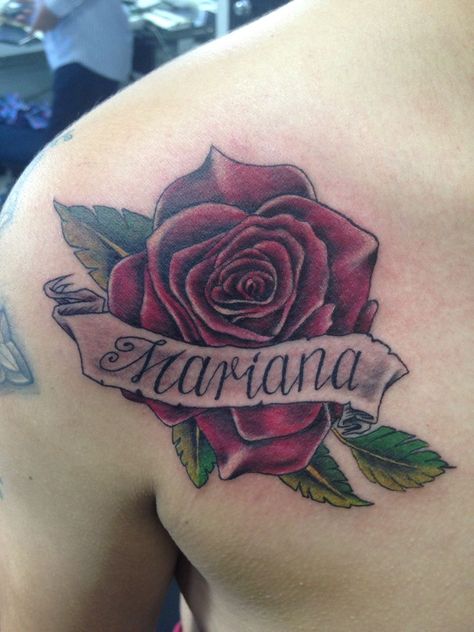 rose tattoo whit the name mariana on it on a ribbon in the shoulder and chest area Roses With Ribbon Tattoo, Name In Rose Tattoo, Rose Name Tattoo Men, Roses With Names Tattoos For Men, Rose With Name Tattoo Design, Rose With Names Tattoo, Rose With Banner Tattoo, Mariana Tattoo, Rose Tattoos With Names