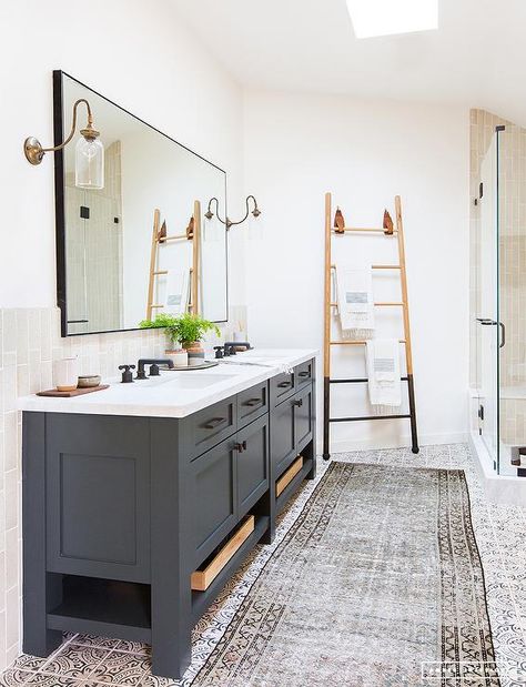 Lit by brass and glass sconces a black framed mirror is mounted above a dark gray dual bath vanity fitted with shelves, oil rubbed bronze hardware and a white quartz countertop finished with sinks paired with oil rubbed bronze faucets. Vintage Bathroom Inspiration, Modern Vintage Bathroom, Gray Vanity, Jillian Harris, Boys Bathroom, Amber Interiors, Studio Mcgee, Bath Room, Vintage Bathroom