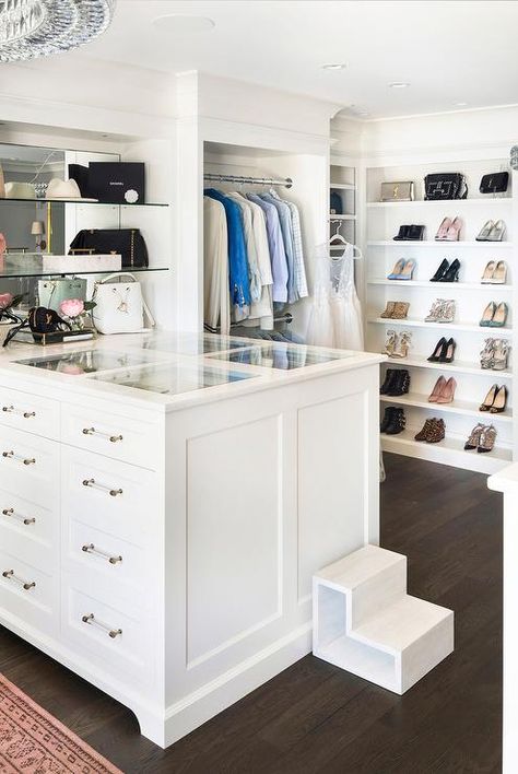 Glass and brass pulls accent a white closet island fitted with a glass top and lit by a crystal chandelier. Restoration Hardware Chandelier, Glam Closet, Closet Island, Cabinets With Glass Doors, White Closet, Beautiful Closets, Walk In Closet Design, Open Cabinets, Dressing Rooms