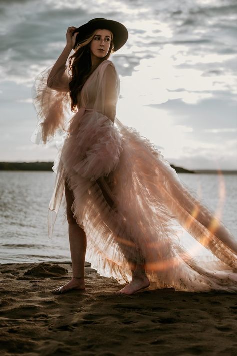 Woman wearing pink tulle robe and a black hat is walking down a beach Tulle Dress Beach Photoshoot, Embodied Woman, Tulle Dress Photoshoot, Photoshoot At The Beach, Wave Photography, White Flowy Dress, Texas Photo, Waves Photography, Puffy Dresses