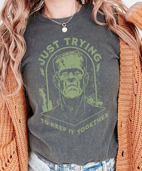 Get ready to keep it spooky and stylish this Halloween with our exclusive 'Just Trying to Keep It Together' Frankenstein Halloween shirt! Perfect for those who love a little Halloween humor, this unique shirt features a distressed Frankenstein design with the quote 'Just Trying to Keep It Together' adorned across the front. Made from soft, high-quality fabric, this shirt offers both comfort and style. Wear it to Halloween parties, trick-or-treating, or simply to celebrate the spirit of the season. Grab yours now and show off your love for Halloween in a fun and fashionable way! Graphic is distressed for a vintage look. Please check the size chart and size up a couple sizes for an oversized look. *The larger the shirt, the larger the graphic.  Our printer sizes the graphics proportionate to Halloween Shirt Ideas For Women, Spooky Fall Outfits, Cricut Halloween Shirt Ideas, Vinyl Halloween Shirts, Frankenstein Tshirt, Cricut Halloween Shirt, Styling Graphic Tees, Halloween Tshirt Ideas, Frankenstein Design