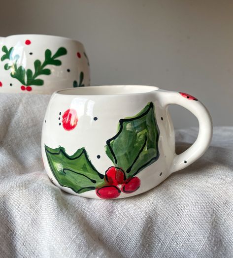 Add a little festivity to your morning brew with our delightful Christmas mugs! Each one is made from a high quality white stoneware clay and carefully handprinted with bright Christmassy colours adding a little extra warmth and charm to your holiday season.  Available in two styles. Holly Berry Under the Mistletoe  Measurements H 7.5cm W 7.5cm Capacity 300ml Please note: Each piece is individually made by hand. Designs and colours may vary slightly from shown in the images due to the making pro Painting Christmas Mugs Ideas, Christmas Mug Pottery Painting, Christmas Cup Painting, Christmas Painted Mug, Christmas Mug Ceramic, Painted Christmas Mugs Diy, Christmas Painted Pottery, Mug Painting Ideas Christmas, Christmas Mug Painting Ideas