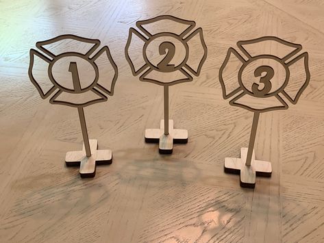 "This listing is for table numbers in the shape of a firefighter seal which are made from 1/8\" wood and are approximately 5\" wide x 8\" tall they come with flat cross stands to keep them upright. The table numbers come left unfinished (natural color). You can paint them any color you like. These table numbers will add the perfect touch to any party décor! **If you need several table numbers, message me for a bulk price :) * These table numbers are made to order. * 5\" Wide x 8\" Tall. * Each t Firefighter Wedding Favors, Fire Banquet Centerpieces, Fireman Wedding Decorations, Firefighter Party Decor, Fire Department Centerpieces, Firefighter Wedding Decorations, Firefighter Centerpiece Ideas, Firefighter Centerpieces, Fire Department Banquet