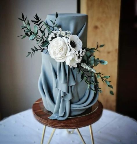 Elegance dusky blue drape cake. Complimented with sugar flowers and foliage Drape Cake, Dusty Blue Elegant Wedding, Wedding Cake Dummies, Wedding Cake With White Flowers, Cake With White Flowers, Dusky Blue Wedding, Blue Elegant Wedding, Art Deco Wedding Cake, Geometric Wedding Cakes