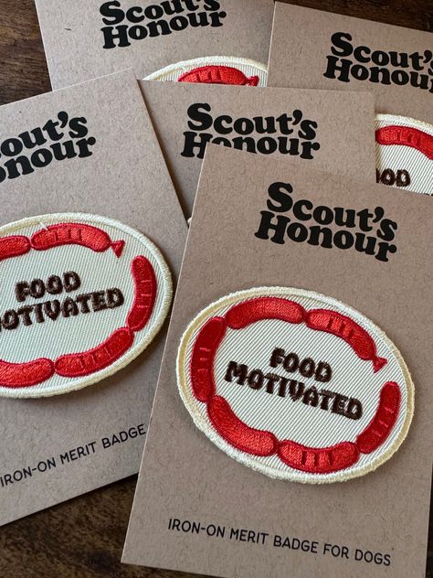 "Does the sight of delicious snacks make your dog weak in the knees? The FOOD MOTIVATED badge is for those dogs who's nose knows no bounds when it comes to tasty treats! Measures approximately 2 1/2\" x 1 3/4\". Oval shaped badge in soft white with dark brown lettering and dark red sausage links around the outer edge. Scout's Honour of the UK makes high quality embroidered patches for your pup's favorite bandana, jacket, vest, harness or sweater.  All of our merit badges are iron-on. It's fuss f Bandana Jacket, Bag Patches, Sausage Links, Merit Badge, Weak In The Knees, Delicious Snacks, Dog Clothing, Jacket Vest, Hoppy Easter