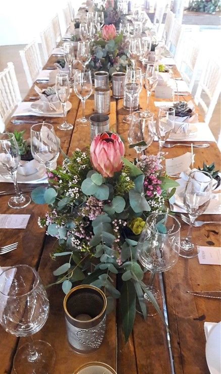 This style of table decor is so popular and looks so beautiful in the form of a table runner. It includes a range of different varieties of proteas, fynbos and greens in separate trays.  #Fynbos #Spring #Flowers #FabulousFynbos Protea Themed Wedding, Protea Wedding Table Decor South Africa, Botanical Wedding Table Decor, Protea Table Decor, Protea Wedding Table Decor, Protea Flower Arrangements, Fynbos Wedding, Fall Wedding Place Settings, Protea Wedding