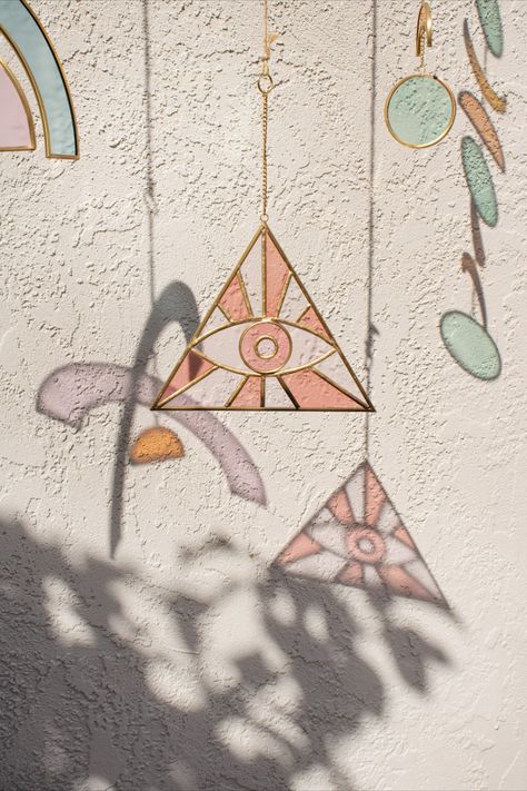 Brighten your window with the auspicious elegance of our triangular stained-glass suncatcher. Handcrafted in India from a mosaic of pink-hued glass pieces in the shape of an evil eye, an ancient symbol thought to keep bad spirits at bay, this brass-accented beauty will catch the light and warm your decor. #worldmarket #suncatcher Evil Eye Suncatcher, Evil Eye Stained Glass Patterns, Stained Glass Eye, Bad Spirits, Glass Evil Eye, Zen Space, Outside Decorations, Feeling Inspired, Glass Designs