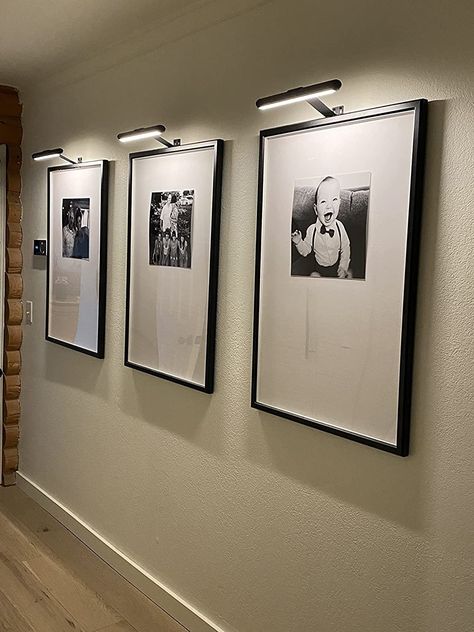 Hallway Photo Wall With Lights, Picture Frames On The Wall With Lights, Artwork Lighting Wall, Wall Light For Painting, Frames On Wall With Lights, Wall Lights With Pictures, Lights Over Pictures Frames, Picture Frame With Light Above, Black And White Photos On Wall Ideas