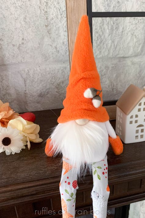 Vertical image of a gnome with a white beard, orange hat, felted acorns, and long legs sitting on a mantle with fall florals and mini ceramic houses. No Sew Gnome, Swedish Gnomes, Gnome Sewing Pattern, Gnome Sewing, Gnome Beard, Gnome Shelf Sitter, Boot Pattern, Fun Fall Decor, Gnome Diy