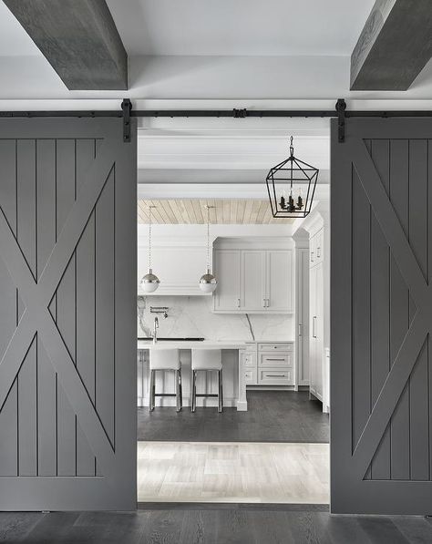 Gray plank barn doors on rails enclose a cottage kitchen with white cabinets, plank walls and dark stained oak wood floors. Dark Stained Wood Floors, White Barn Door, Kitchen Transitional, Cottage Style Kitchen, Wood Barn Door, Rustic Barn Door, Oak Wood Floors, Grey Doors, Plank Walls