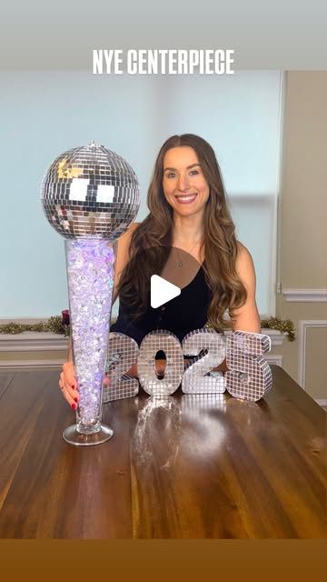 Kaitlyn Anderson on Instagram: "NYE CENTERPIECE 🪩 This DIY only takes a few supplies and turns out so cool! Why is it kinda giving Super Bowl Champ lol

🔗Shop the video on my LTK & Amazon!

SUPPLIES:
-Tall glass vase
-Clear gems
-String lights
-Disco ball

DIRECTIONS:
1. Gather string lights together to make a long hot dog shape and hold in the middle of the vase.
2. Pour gems around lights and place battery pack at the top hiding them with more gems.
3.  Place disco ball on top and set out as a statement centerpiece for NYE!

#nye #nyeparty #newyear #newyearseve #newyearsdecor #newyearseveparty #nyeparty #nyepartyideas #discodecor #discoball #discoparty #nyecenterpiece #2025 #2025ideas #newyearsideas"