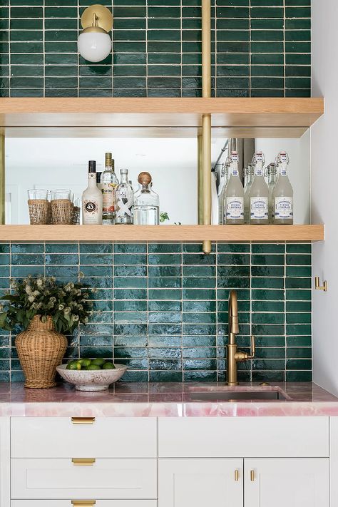 A brass and white glass globe pendant is mounted to jade green stacked backsplash tiles over brown and gold shelves mounted flanking a mirrored backsplash and over a sink with a brushed gold faucet. Pink Stone Countertops, Pink Countertops Kitchen, Pink Marble Countertops, Pink Granite Countertops, Pink Countertops, Laundry Flooring, Arch Tile, 1970s House Renovation, Wet Bar Backsplash