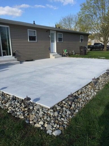 River Rock Around Concrete Patio, Rock Borders Edging Around Patio, Rock Around Patio Ideas, Concrete Patio With Rock Border, River Rock Around Patio, River Rock Patio Border, Rock Around Deck, Rock Border Around Concrete Patio, Simple Concrete Patio Ideas On A Budget