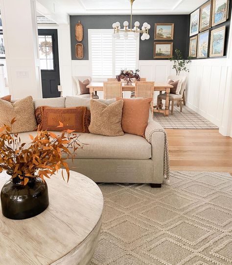 Orange throw pillows decorate a beige couch seated on a beige braided diamond pattern area rug. The couch is paired with a whitewashed wood drum coffee table in this living room next to the dining room. Curtains To Match Tan Couch, Pillows For Orange Couch, Couch Pillows For Tan Couch, Beige Microfiber Couch Living Rooms, Sandy Couch Living Room, Brown Couches With White Pillows, Beige Gray Couch Living Room, Grey And Beige Couch Living Room, Neutral Orange Living Room