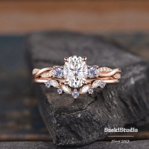 "Oval Moissanite Alexandrite Cluster Moissanite Ring Rose Gold Engagement Ring Set 2pcs Three Stone Twist Bridal Set Diamond Ring Vine Ring  ITEM INFORMATION Metal Type - Solid 14k Rose Gold, yellow gold, or white gold  Band Width - (approx. 1.8mm) Center Stone - 6x8mm Moissanite, Oval Clarity - VVS Color -  D-E-F Side Stone - moissanite or diamonds can be selected. Side stone - lab alexandrite  **Stone Replacement** Available with any other gemstones, please feel free to contact me for a quote. **Metal Type** Available in 14K or 18K yellow gold, white gold, and rose gold. Please select from the drop-downtown menu. **Production Time& Rush Order** Our standard production time is 3-4 weeks from the time of purchase. I am very happy to provide rush order service, the price and s $60, the Proc Unique Engagement Rings Nature Inspired, Rose Gold Engagement Ring Twisted Band, Rose Gold Three Stone Engagement Ring, Alexandrite Moissanite Ring, Diamond And Pearl Ring Engagement, Two Piece Wedding Ring, Twist Engagement Rings With Wedding Band, Enchanted Engagement Ring, Engagement Rings For Fat Fingers