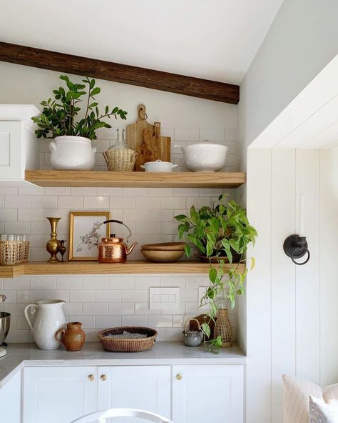 Wood floating shelves are used to create a carefully arranged display in this kitchen. White subway tile covers the walls over white shaker cabinets with gold hardware. Potted plants sit on the shelves among wood kitchen items and vintage dГ©cor. Diy Open Shelving Kitchen, Kombuis Idees, Kitchen Shelf Design, Laundry Diy, Shelving Decor, Floating Kitchen Shelves, Kitchen Floating Shelves, Open Cabinet, Kitchen Shelving