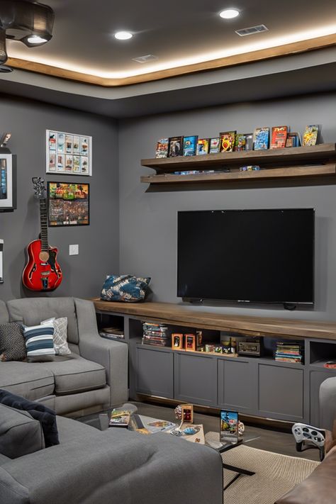 Modern entertainment room with a large TV, shelves holding video games and memorabilia, a red guitar on the wall, and a gray sectional sofa. Teenage Games Room, Loft Gaming Room, Kids Video Game Room, Alternative Formal Dining Room, Basement Game Room Ideas Family, Multiple Tv Wall Ideas, Tv Gaming Room, Gamer Living Room Ideas, Teen Game Room