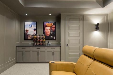 Framed movie poster hang from paneled taupe basement walls and are lit by recessed lights fixed to a taupe ceiling over a candy station. Taupe Ceiling, Herringbone Brick Floor, Transitional Basement, Basement Movie Room, Movie Frames, Grey Ceiling, Tan Pillows, Blue Sectional, Recessed Lights