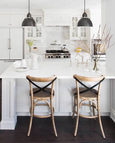 On dark hardwood floors, two french cafe bar stools with leather x-back straps sit in front of a gorgeous white peninsula topped with white quartz countertops and fitted with a deck mount vintage faucet accenting an undermout kitchen sink illuminated by two industrial black pendants. Cafe Bar Stools, Black And White Furniture, White Kitchen Island, Stools For Kitchen Island, White Interior Design, Bar Stools With Backs, Home Luxury, Transitional Kitchen, Trendy Kitchen