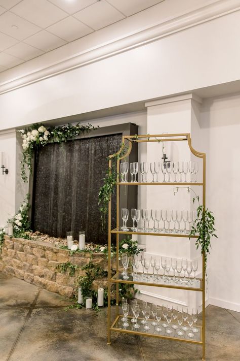 This image features a gold champagne rack for a wedding cocktail hour and entrance. The stand is accented with greenery and next to a water wall with candles, white blooms and greenery. Greenery For Wedding, Candles White, Photography Location, Wedding Entrance, Gold Champagne, Champagne Wedding, Location Photography, Greenery Wedding, Champagne Gold