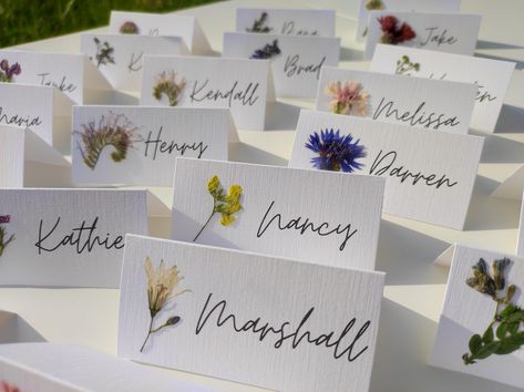 Each card has its own meadow flower, real pressed flower carefully glued on. The cards are already folded and ready to be placed on the table. Perfect for nature inspired wedding, dried flowers wedding, Rustic weddings. White, matte, decorative paper, 250 gsm, is used. You can choose a folded card or a flat card. -The size of a folded card is 9X4.5cm, 3.5X1.7 inches (Full size unfolded 9X9 cm, 3.5X3.5 inches). I can make cards with name and surname. -Flat card size: 9X4.5cm, 3.5X1.7 inches - Tag with golden hole and whatever text you want  size: 10X5 cm, 3.9X1.9 inches.  If you have any special requirements please write to me. Orders over 70 pieces have FREE & EXPRESS SHIPPING. Look here:   https://www.etsy.com/listing/1487518143/pressed-flower-place-cards-with-real?click_key=eca58308b3f2a Wedding Seating Chart Pressed Flowers, Dried Flower Name Card, Pressed Flowers Name Card, Name Cards Table Settings, Fun Place Cards Wedding, Whimsical Place Setting, Name Tag Table Setting, Spring Wedding Name Place Cards, Wedding Invitation With Dried Flowers