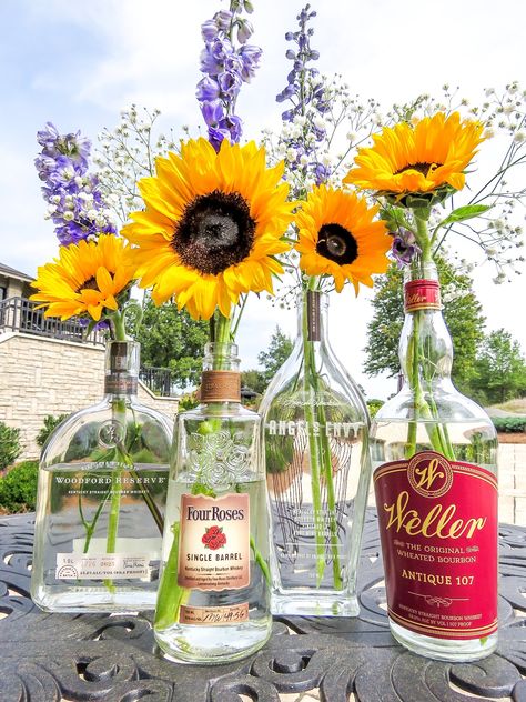 Bourbon Bottle Centerpieces for a "Whiskey & Wildflowers" event theme. Sunflowers, baby's breath, and purple delphiniums. #centerpieces #bourbon #wildflowers #whiskey #eventdesign Bourbon Bottle Vase, Centerpieces With Liquor Bottles, Whiskey And Wine Wedding Theme, Bourbon Wedding Centerpieces, Bourbon Event Decor, Bourbon Bottles Wedding, Flowers In Bourbon Bottles, Whiskey And Wine Wedding, Whiskey Themed Centerpieces