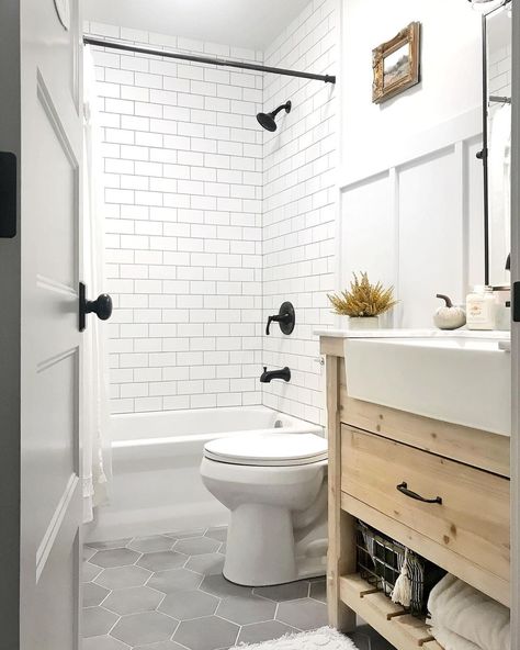 White tub and shower combo clad in white subway tile is fitted with a black faucet kit. A white toilet in front of the shower stands next to a light wood washstand in this gray hexagon floor tile bathroom. Hexagon Tile Bathroom Floor, Hexagon Tile Bathroom, White Subway Tile Shower, Grey Bathroom Floor, Tile Bathrooms, White Subway Tile Bathroom, Subway Tile Showers, Hexagon Tile Floor, Grey Bathroom Tiles