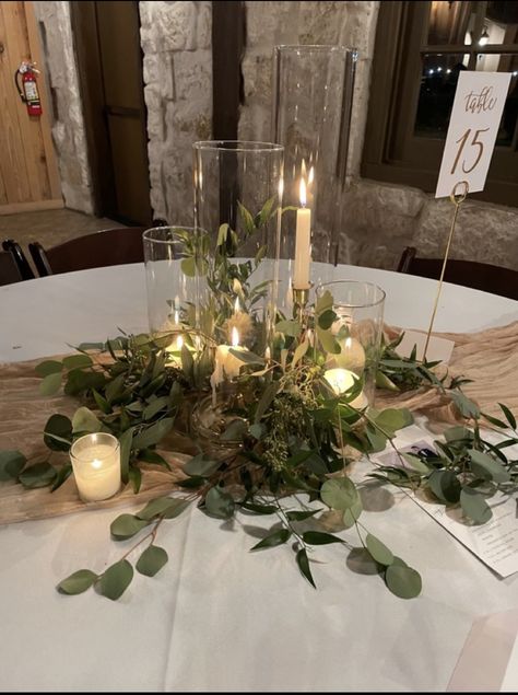 Candle And Glass Centerpieces, Greenery Wedding Circle Table, Eucalyptus Wedding Circle Table, Eucalyptus And Gold Wedding Table Decor, Dark Green Wedding Details, Wedding Table Flowers With Candles, Candles For Centerpieces Wedding, Wedding Tablescapes Round Rustic, Greenery On Black Tablecloth