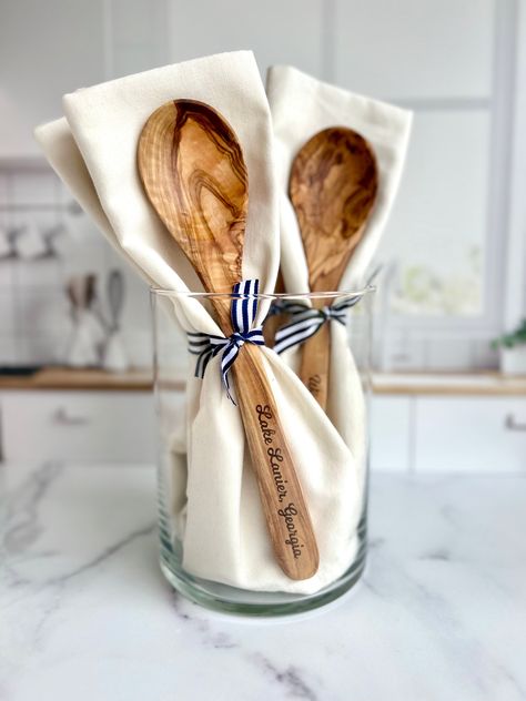 Introducing your new favorite kitchen addition: the Custom-Lake-Name Engraved Olive Wood Spoon and Towel set! This isn't just your average kitchenware - it's a piece of home. Beautifully engraved with your beloved lake, beach, or river name, it's made to bring memories straight into your kitchen. It's a gift that resonates with both men and women, perfect for housewarming or as a lovely hostess present. Imagine commemorating a special time with this personalized kitchen set, made to fit right into your lake house, beach house, or even your cozy little kitchen in the suburbs. Here's what makes this spoon and towel set a cut above the rest: - This custom engraved spoon, carved from Mediterranean olive wood, brings a touch of nature to your kitchen. - The natural (undyed) plain-woven 100% cot Personalized Kitchen Items, Wood Spoon Crafts, Hostess Gift Ideas House Guests, River Name, Hummingbird Designs, Small Hostess Gifts, House Warming Gift Ideas, Kitchen Gift Baskets, Laser Christmas