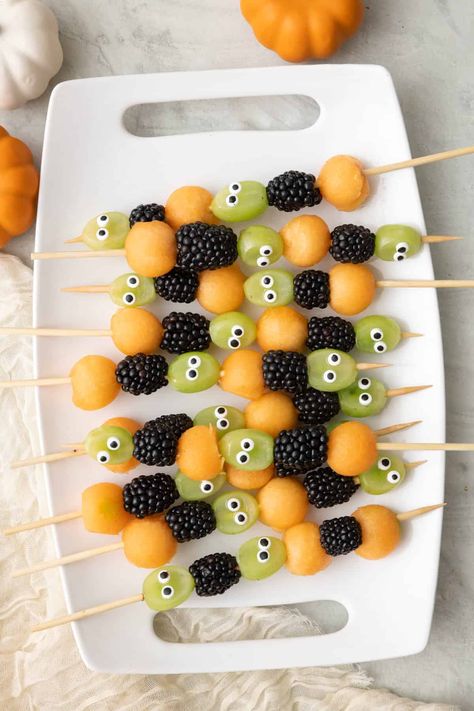 Get ready to spookify your taste buds with our Halloween Fruit Kabobs! These ghoulishly delightful skewers feature juicy cantaloupe balls that are like mini pumpkin orbs, grapes with mischievous googly eyes that seem to watch your every move, and plump, mysterious blackberries that add a dark twist to your fruit adventure. It's a fruity fiesta that's as playful as it is eerie – the perfect way to haunt your taste buds this Halloween! Grab one and take a bite, if you dare! | Halloween F Fruit Skewers Halloween, Halloween Fruit Class Party, Grape Halloween Snack, Fruit Kabobs Halloween, Pumpkin With Fruit Skewers, Spooky Fruit Salad, Fruit Halloween Tray, Halloween Fruit Kabobs For Kids, Halloween Kabobs For Kids