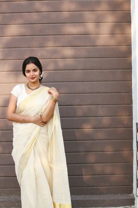 A traditional style Karala Kasavu Saree styled with a plain off white blouse, Firangipani flowers on the hair, a dull gold necklace and reddish maroon on the lips Kerala Traditional Saree, Kerala Kasavu Saree, Saree Shoot, Cream Saree, Phulkari Saree, Baluchari Saree, Onam Saree, Savage Wallpapers, Off White Blouse