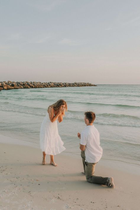 Young couple dressed in white & neutral summer clothing - on shore of beach in St Andrews State Park, PCB Florida.  Young man is kneeled down on one knee, with ring outstretched, girl is excitedly covering her face with her hands. Photo taken by intimate wedding & portrait photographer Brittney Stanley of Be Seen Photos Propose On The Beach, Simple Proposal Ideas Beach, Beach Engagement Surprise, Surprise Proposal Photoshoot Beach, Marriage Proposal Beach, Engagement At The Beach, Surprise Beach Engagement, Florida Proposal Ideas, Engagement Proposal Ideas Beach