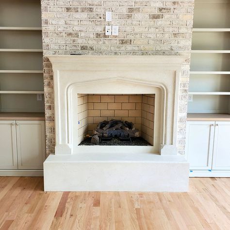 A gothic stone fireplace mantel sits atop an oversized hearth made of the same cream-colored cast stone material. The fireplace is surrounded by built-in cabinets with white oak counters and shelving running up the height of the fireplace wall. The cast stone is complimented by a light-colored brick that encapsulates the fireplace chase or protrusion. Fireplace Hearths, Fireplace Mantel Surround, Fireplace Mantel Surrounds, Stone Fireplace Mantel, Stone Fireplace Surround, Mantel Surround, Fireplace Hearth, Gorgeous Bedrooms, Fireplace Surround