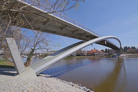 The pedestrian and cyclist bridge, which is situated between the city’s historic center and town suburb ‘Zálabí’, connects cycling and pedestrian trails running along both banks of the river. Since it is located near a historic arch bridge, it is also formed by an arch structure, but it has a longer span and it has no supports in the river. The bridge structure consists of two outwardly inclined steel arches, on which a bridge deck from prestressed concrete is suspended. The rise of the arches w Arch Structure, Bridges Architecture, Bridge Support, Bridge Structure, Steel Bridge, Arch Bridge, Pedestrian Bridge, Bridge Design, A Bridge