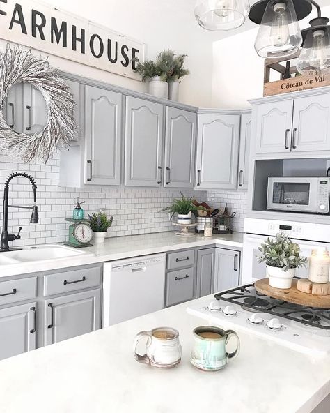 This kitchen features white walls, light grey cabinets with black handles, and white counters. Potted plants in white pots are strewn about the kitchen in front of the white subway tile backsplash with a light grey grout. Grey Cabinets White Countertops, Cabinets With Black Handles, Light Grey Cabinets, White Kitchen Counters, Gray Grout, Light Grey Kitchen Cabinets, Grey Kitchen Walls, Light Grey Kitchens, Grey Kitchen Floor