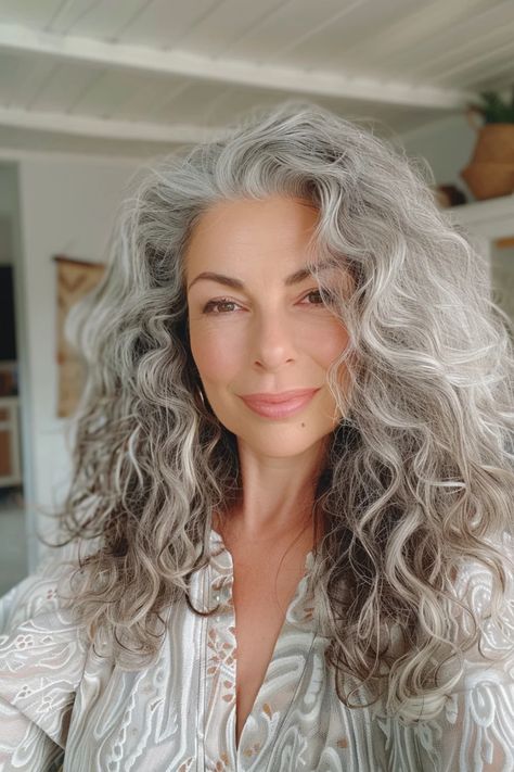 Smiling woman with long, curly gray hair and a patterned blouse in a bright room. Long Gray Hair Over 60 Older Women, Grey Hair Inspiration Aging Gracefully, Curly Salt And Pepper Hair, Trendy Grey Hair, Salt And Pepper Hair Women, Curly Gray Hairstyles, Short Curly Gray Hair, Grey Wavy Hair, Curly Gray Hair Over 50