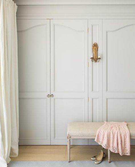 Chic, French closet feature slight gray wardrobe closet doors illuminated by a gold leaf sconce alongside a cream linen French bench. European Country Home, Gray Closet, French Closet Doors, Grey Wardrobe, Patina Farm, Patina Style, French Wardrobe, Armoire Dressing, Slaap Lekker