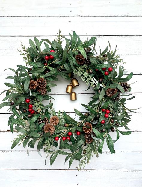 Dress up your door this holiday season with this olive branch and evergreen Christmas wreath! This wreath is carefully handmade using high quality faux olive branches, cedar, real pinecones, matte red berries and adorned with four gold bells hanging from the center of the wreath. This beautiful wreath will complement any space. Give your front door or entryway a makeover this holiday season and create a warm and festive atmosphere for you and your loved ones to enjoy. Olive Branch Wreath With Bow, Fresh Foliage Christmas Wreaths, Faux Olive Branches, Christmas Red Berry Wreath, Ivy Christmas Wreath, Red Berry Wreath, Evergreen Christmas, Olive Branches, Matte Red