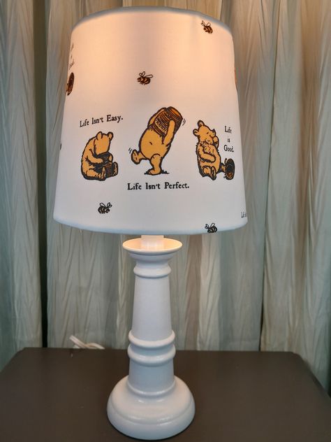 This adorable Winnie the Pooh lamp features an upholstered shade with a cotton sateen fabric that depicts Winnie the Pooh with little sayings scattered throughout. The shade fits on any lamp base, sitting on the socket above the light bulb on a suspended ring. The shade itself measures 6 and 3/4 in long by 7 and 1/2 in wide and fits a base up to 12 in in height. The shades can be purchased alone, or with the lamp base. The assembled lamp offered stands 15 in tall. The hand-painted and sealed base is offered in white or cream. Base color options can be viewed in the photo gallery. What a delightful addition this would be in any baby's nursery or any small child bedroom. Winnie The Pooh Themed Room, Winnie The Pooh Baby Shower Gifts, Winnie The Pooh Room Decor, Winnie The Pooh Kids Room, Winnie The Pooh Rug, Winnie The Pooh Nursery Boy, Neutral Baby Disney Room, Nursery Ideas Winnie The Pooh, Up Themed Nursery Disney