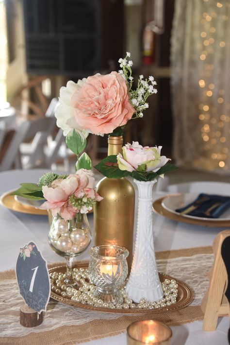 Vintage, elegant, centerpiece.  milk glass, gold wine bottle, pearls, wine glass, peach rose, pink peony, babies breath, navy blue napkin, gold charger, Wishing Well Barn Vintage Wedding Centerpieces Pearls, Vintage Wedding Centerpieces, Blue Wedding Centerpieces, Pearl Centerpiece, Wine Bottle Centerpieces, Vintage Wedding Table, Boda Diy, Bottle Centerpieces, Wedding Bottles