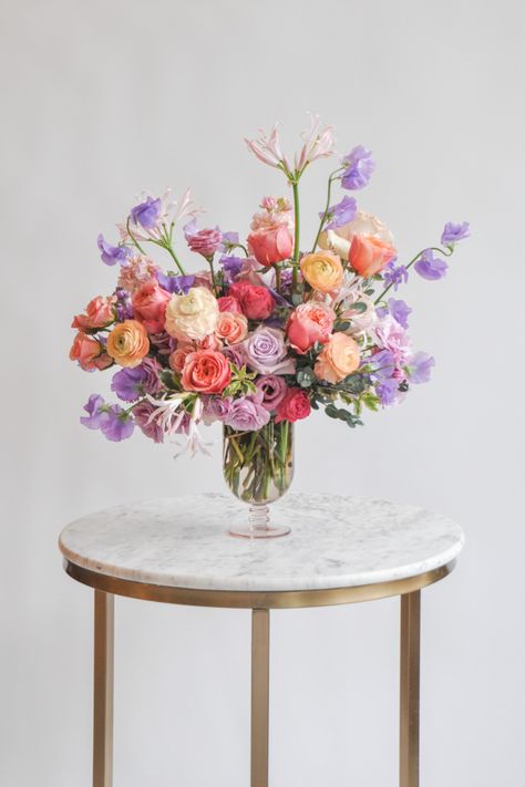 photo of a pastel pink purple and peach valentine's floral arrangement on a marble and gold table in front of a white background Purple Flower Arrangements, Ranunculus Bouquet, Tulips Arrangement, Send Love, Purple Wedding Flowers, Pink And Purple Flowers, Peach Flowers, Pink Bouquet, Peach Roses