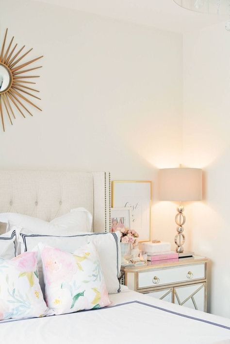 Create a relaxing space to drift off in by using pale throws, soft lighting, + a blush accent. White Gold And Pink Bedroom, Gold And Pink Bedroom, Amazing Mirrors, Nightstand Round, Feminine Bedroom Decor, Spring Bedroom Decor, Mirrors Design, Bedroom Mirrors, Floral Wallpaper Bedroom