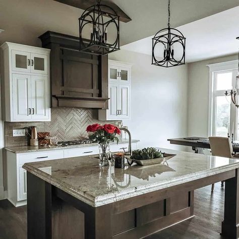 A gray herringbone tile backsplash is installed between white kitchen cabinets and wood hood. Red roses and a metal tray of foliage are utilized as ideas for kitchen island centerpieces. The centerpieces are placed on the gray granite countertop of a wood island...   Image: our_rustic_farmhouse Kitchen Island Centerpieces, Kitchen Island Centerpiece Ideas, Gray Herringbone Tile, Kitchen Island Centerpiece, Kitchen Island Decor Ideas, Wood Hood, Woven Bar Stools, Herringbone Tile Backsplash, Gray Granite