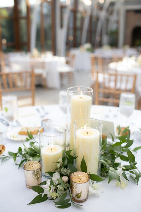 Candle Centerpiece at Romantic Orangerie at Tower Hill Botanic Garden Massachusetts Wedding #weddings #wedding #weddingplanning #weddingflowers #floraldesign Greenery And Candles Centerpieces, Candle Floral Arrangements, Candle With Greenery Centerpiece, Wedding Pillar Candle Centerpieces, Wedding Table Pillar Candles, White Flower Candle Centerpieces, Floral And Candle Centerpiece Wedding Round Table, Candles And Greenery Centerpiece Round Table, Wedding Candle Arrangements