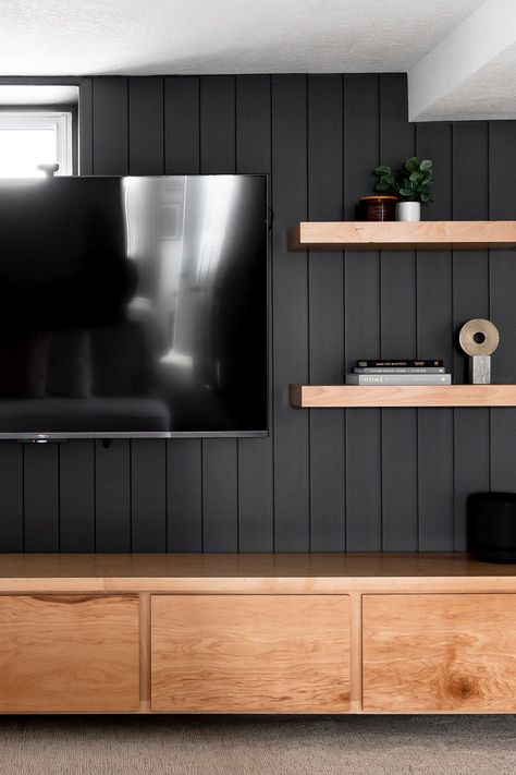 modern traditional basement design dark wall wood shelves Low Profile Tv Wall, Vertical Shiplap Tv Accent Wall, Wide Slat Wall, Tv Wall Man Cave, Wood Panel Wall Behind Tv, Basement Tv Area Ideas, Paneled Tv Wall, Tv Wall Black And Wood, Black Pipe Tv Wall