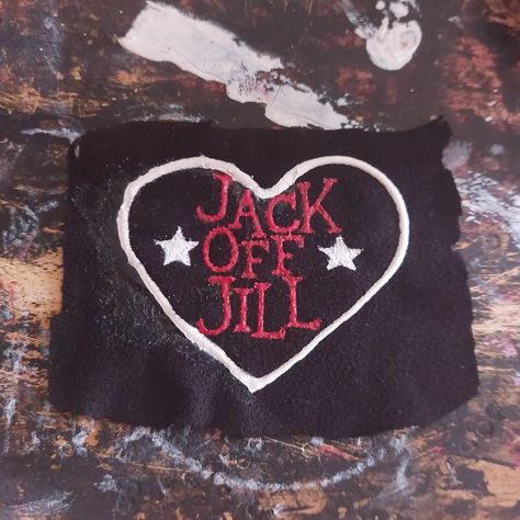 An unevenly cut, black, rectangle, fabric patch is on a paint-stained background. On the patch is a white heart, inside the heart, written in red, are the words "Jack Off Jill" in a vertical column. On either side of the word "Off" are white stars. Jack Off Jill Logo, Punk Shirts Diy, Punk Pins And Patches, Punk Band Patches, Band Patches Diy, Jack Off Jill Band, Punk Patch Ideas, Patch Ideas Punk, Crust Patches