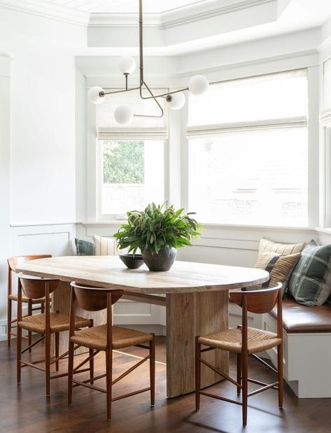 A white built-in bay window dining bench is accented with a brown wooden cushion and placed beneath bay windows dressed in white curtains. Built In Bench Dining Room, Amber Interiors Dining Room, Amber Interiors Dining, Built In Dining Bench, Modern Bay Window, Banquette Dining, Transitional Dining Room, Dining Room Windows, Amber Interiors