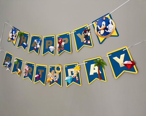 "This handmade Sonic the Hedgehog Happy Birthday Banner is PERFECT for your Sonic-themed birthday party! This banner is made to order with high-quality cardstock and beautifully printed images adhered with foam tape for a 3D effect.  Banners can be personalized with age and name, please make sure to include all personalizations in the notes section including: Name: Age: Date Needed: Banner measures approximately 3.5' to 4 ft wide depending on how pieces are arranged. Each pennant is approximately 4\"x 5\" and comes pre-strung with plenty of ribbon for hanging.  Current lead times are approximately 3-5 days from the order date. If an item is needed more urgently please send me a message and I will do my best to accommodate you. Please note that shades and textures of cardstock may vary due Sonic The Hedgehog Banner, Sonic Birthday Decorations, Sonic The Hedgehog Birthday Party, Sonic Birthday Party, Sonic Birthday Parties, Diy Birthday Banner, Sonic Party, Hedgehog Birthday, Sonic Birthday